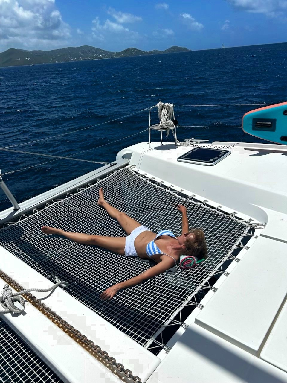 A guest lounging on the catamaran's trampoline net over deep blue water