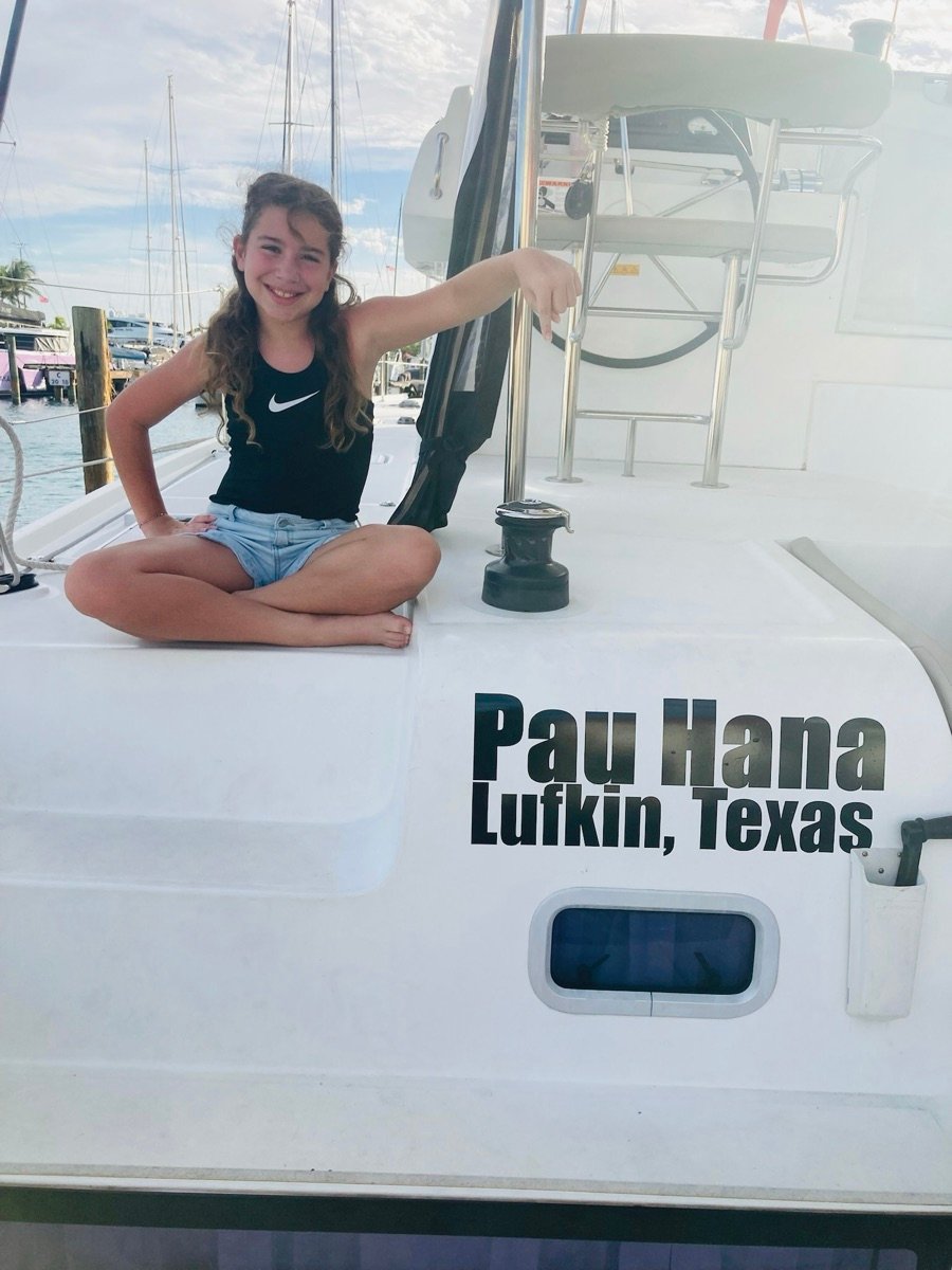A young guest pointing to the Pau Hana, Lufkin Texas name on the catamaran's hull at the dock