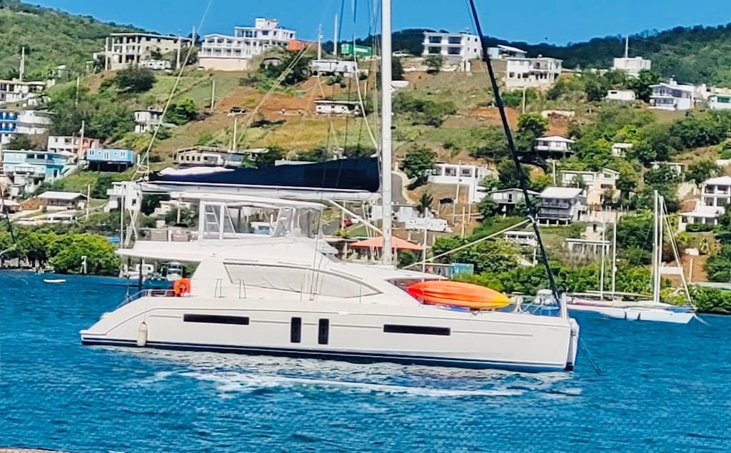 GrooVI, a 58-foot Leopard sailing catamaran, in profile on the bright blue water off St. Thomas, with a hillside of colorful Caribbean homes behind