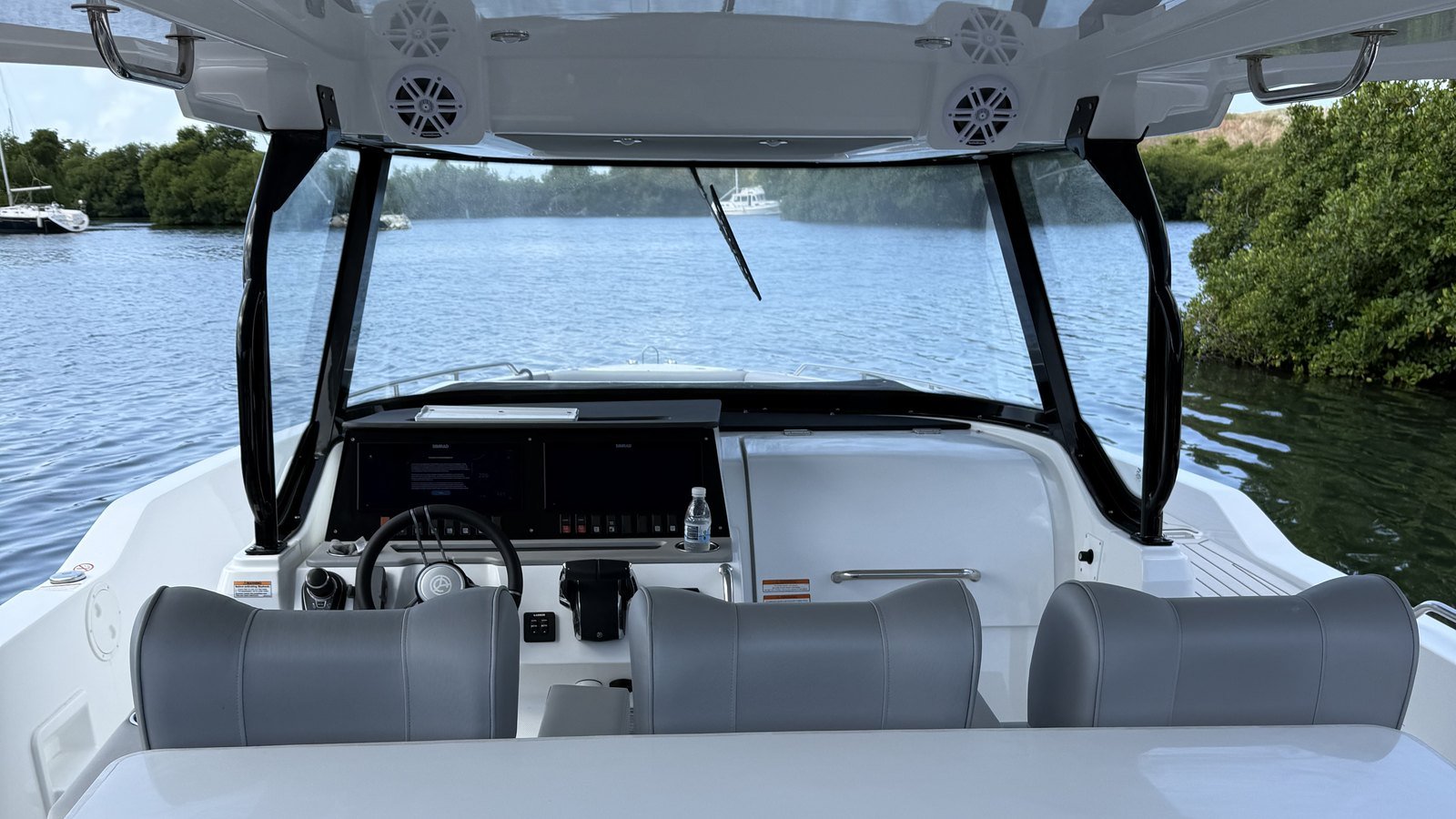 Venture VI at the dock in St. Thomas, looking forward past the helm seats to the twin displays, wheel and hardtop, with calm water beyond the windscreen